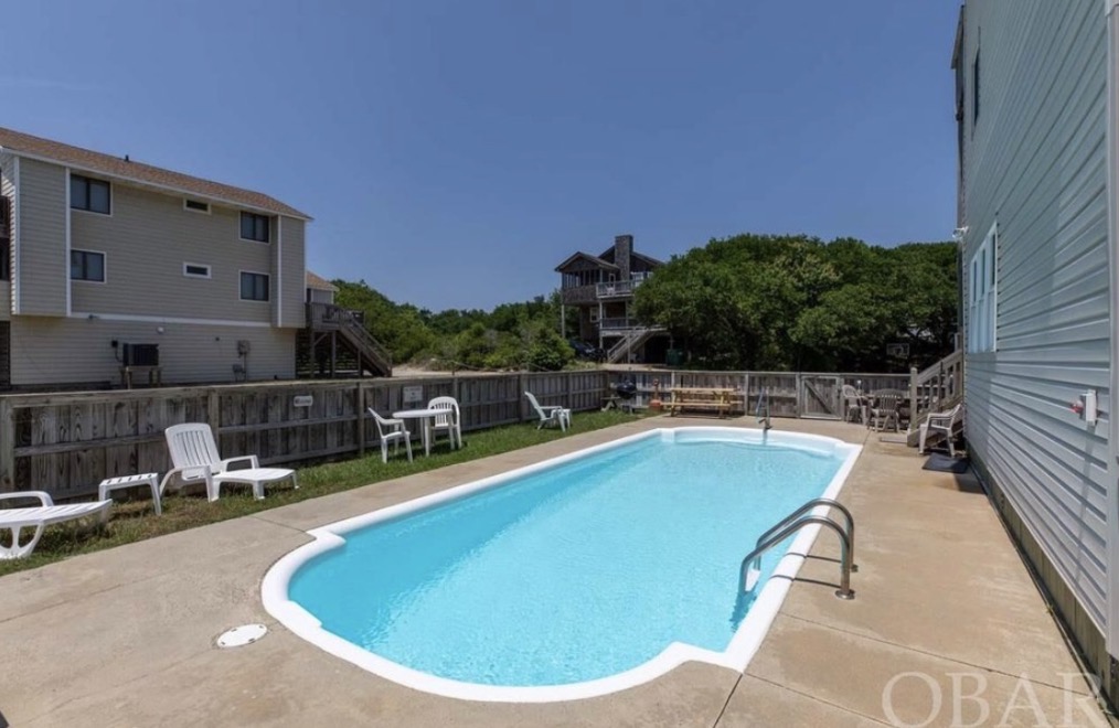 A sunlit swimming pool with lounge chairs and a surrounding deck.