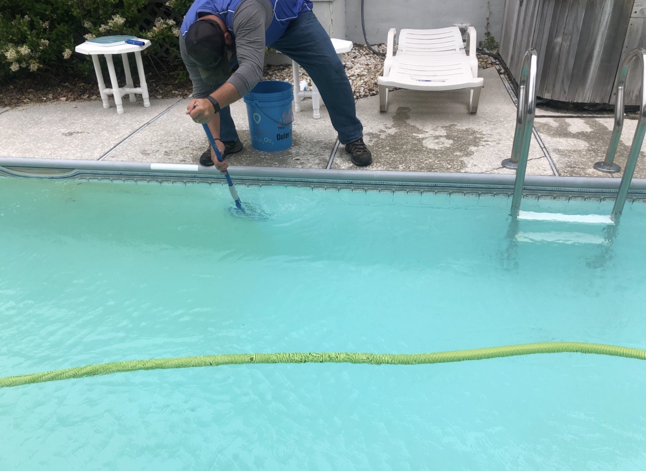 A worker vacuums a swimming pool from the deck.