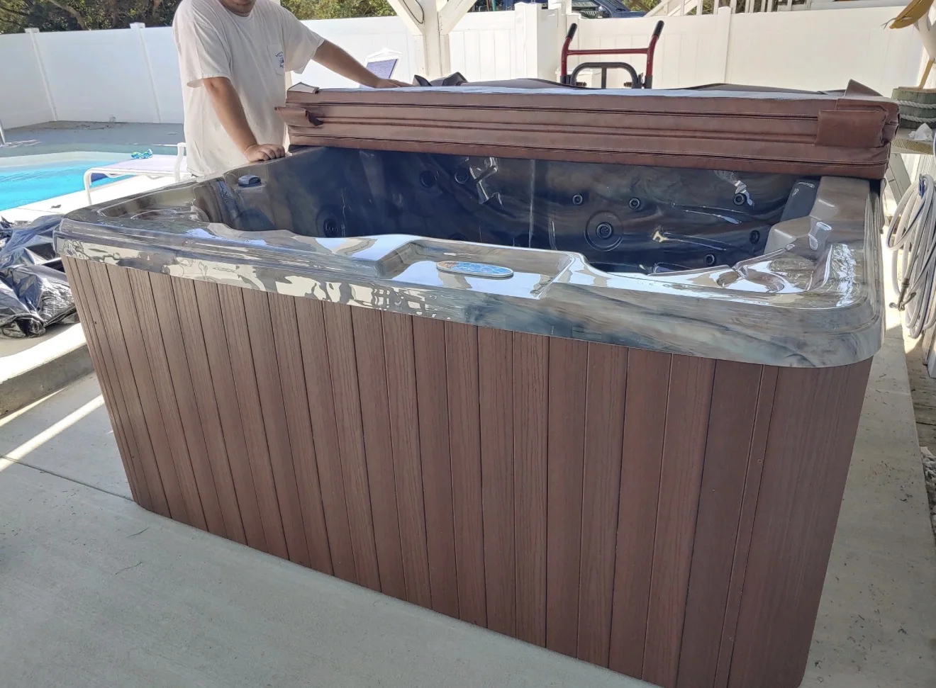 Open hot tub with a wood-finish cabinet beside a swimming pool